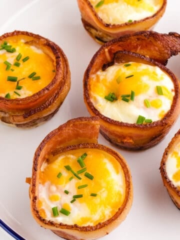 bacon wrapped egg muffins on a white plate with blue trim garnished with parsley