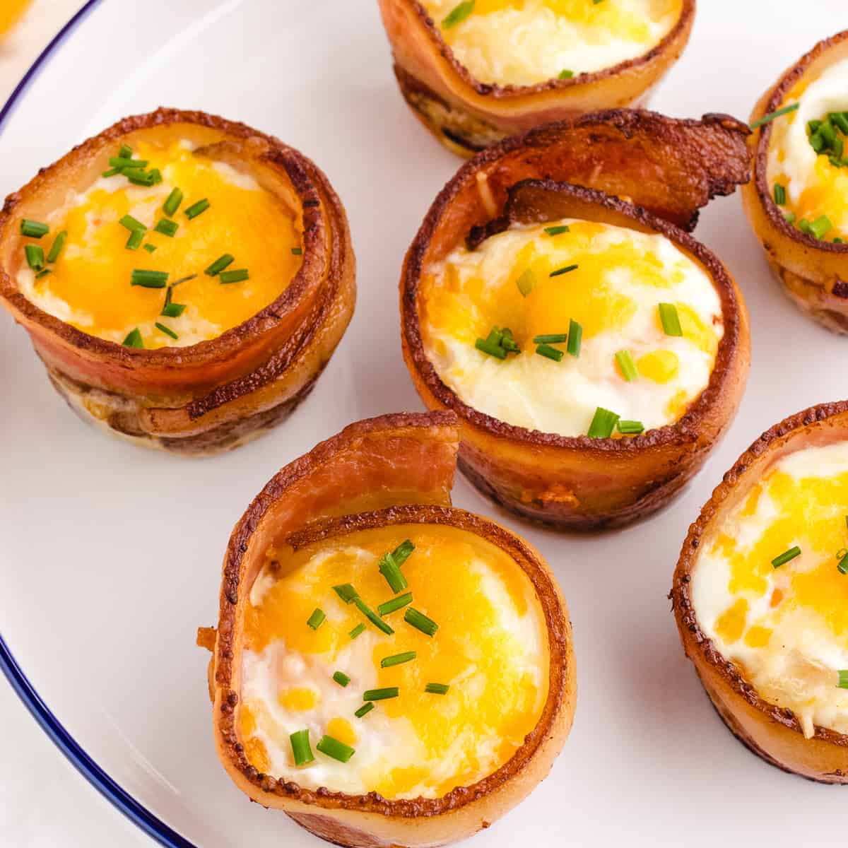 bacon wrapped egg muffins on a white plate with blue trim garnished with parsley