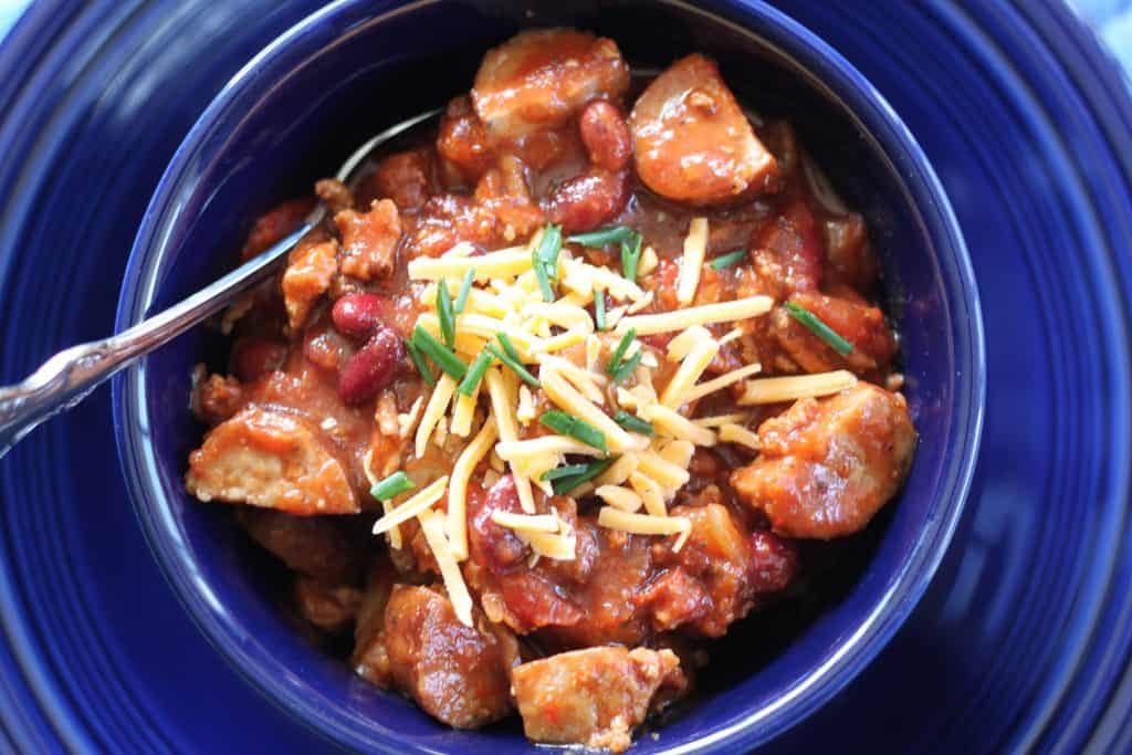 kielbasa chili with sausage and ground beef in a blue bowl with a cheese garnish