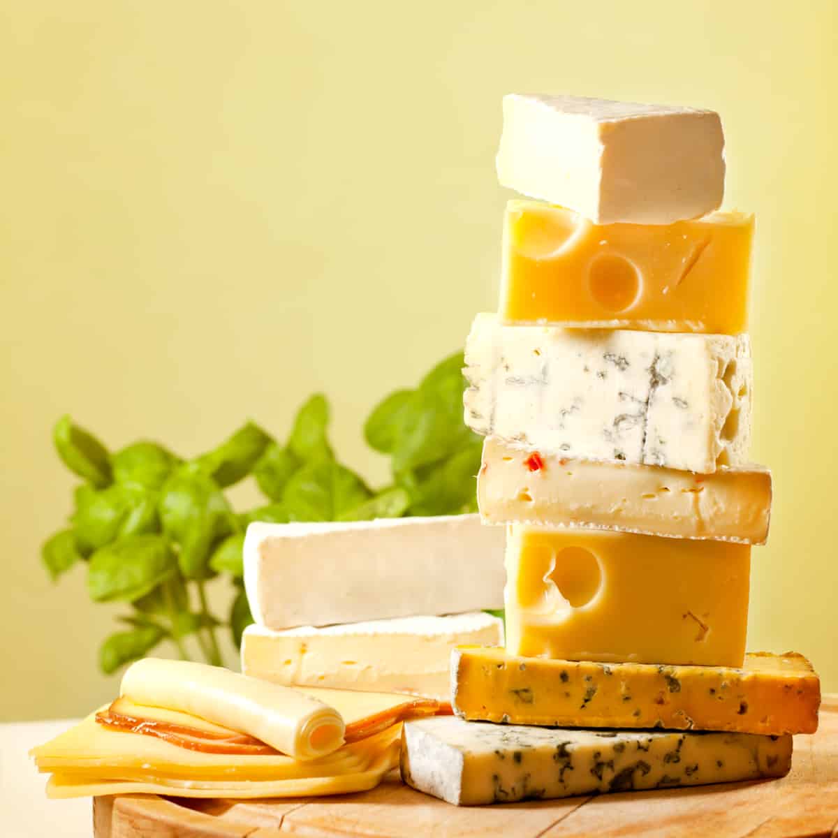 a variety of cheese stacked on a cutting board