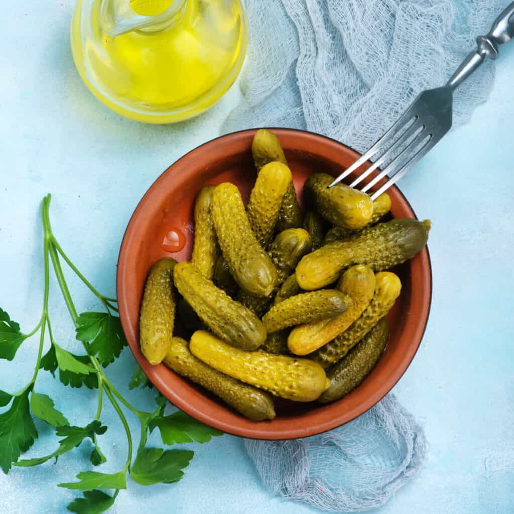 dill pickles in a wooden bowl on a light blue background
