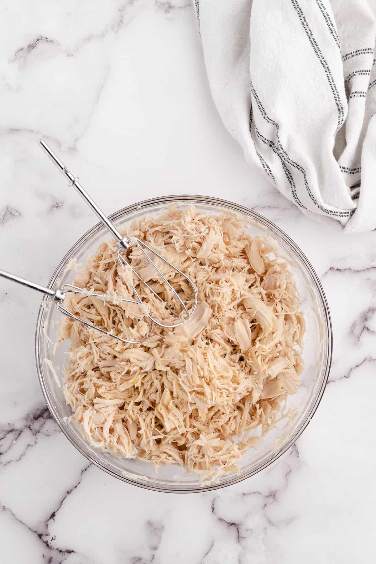 how to shred chicken with hand mixer in a glass bowl on a marble counter top