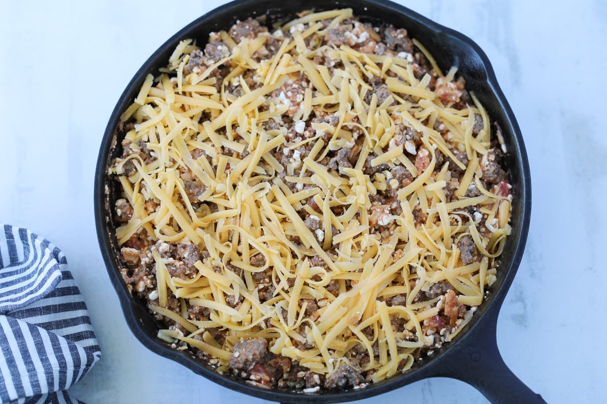 assembling the low carb taco casserole in a cast iron skillet before baking