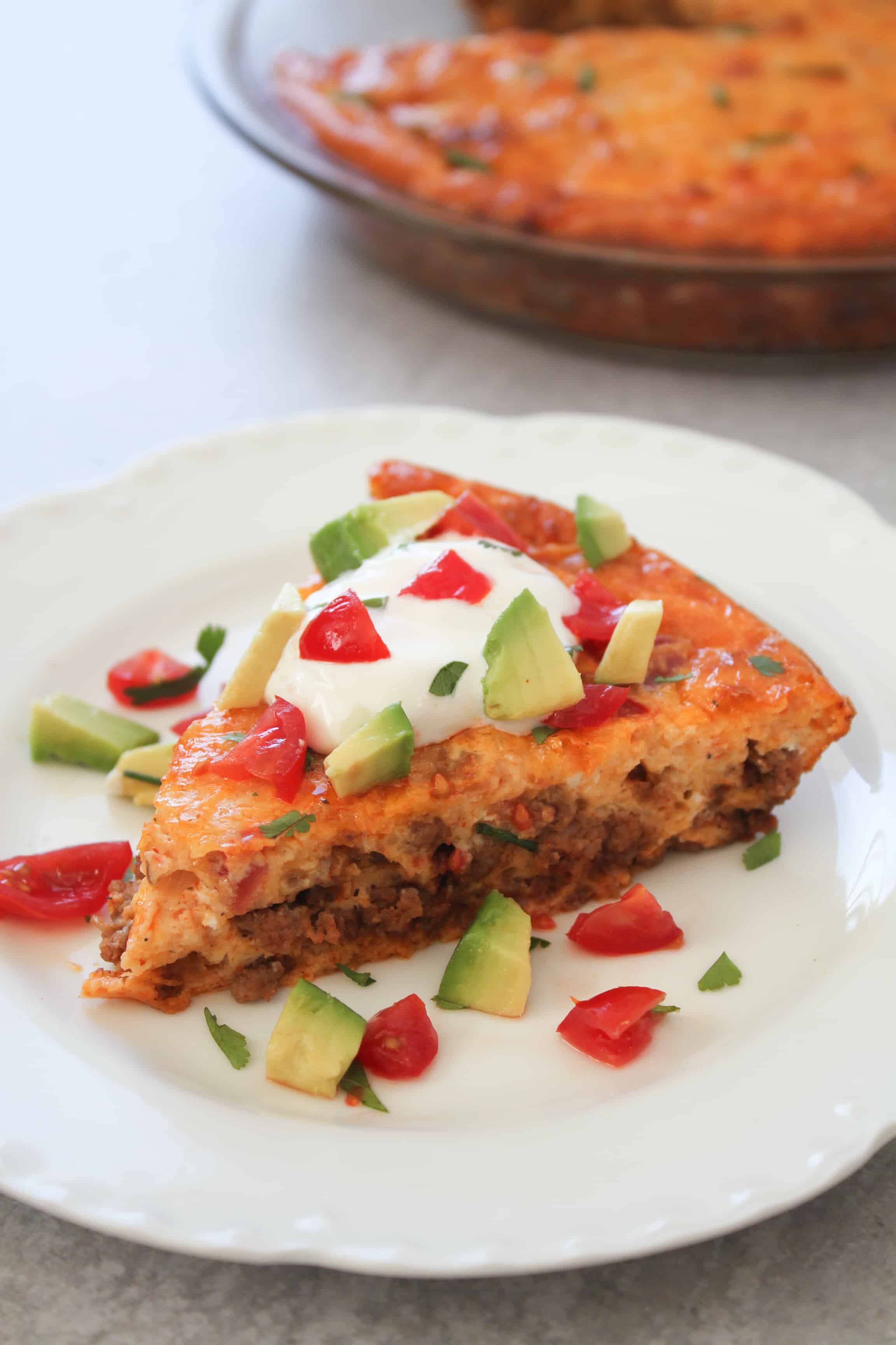 one slice of keto taco pie on a white plate with garnishes