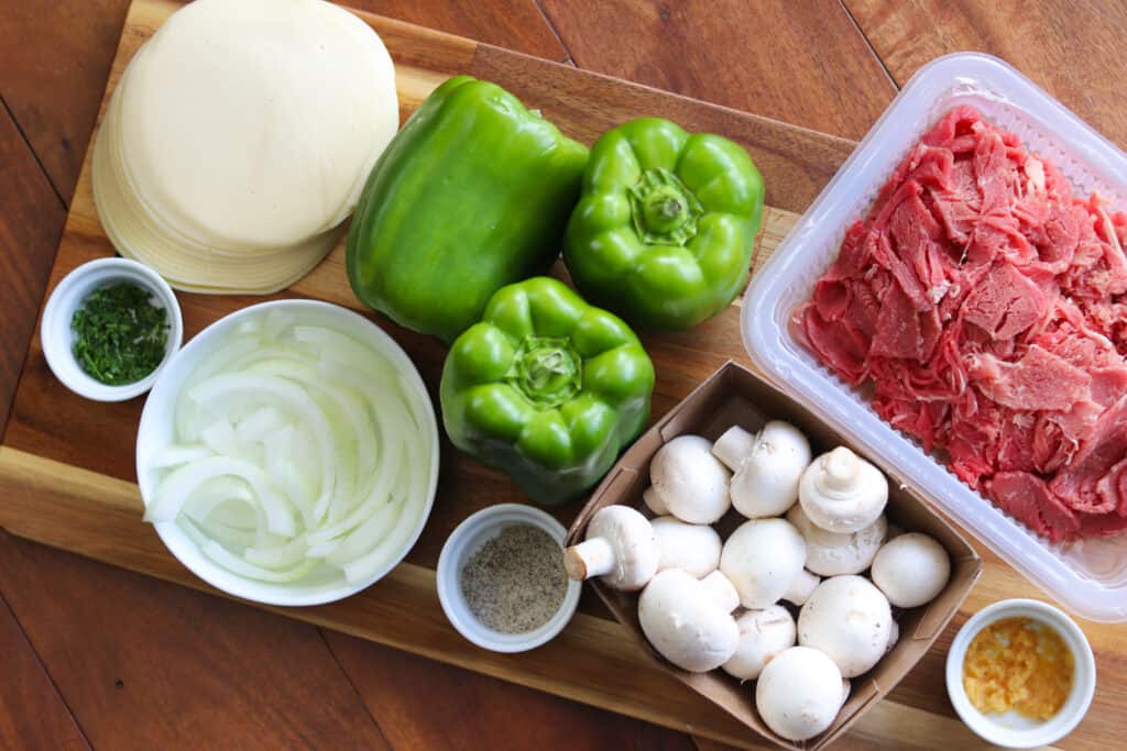 Philly cheesesteak stuffed bell peppers ingredients displayed on a cutting board