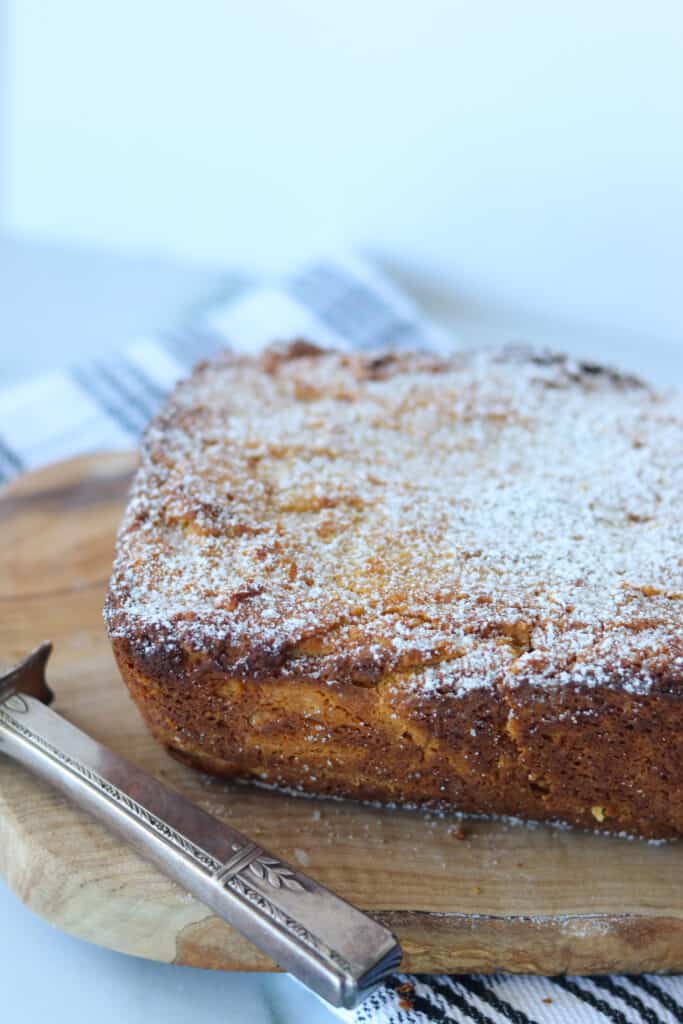 a whole loaf of cooked keto pumpkin cream cheese bread sprinkled with powdered sweetener on a cutting board