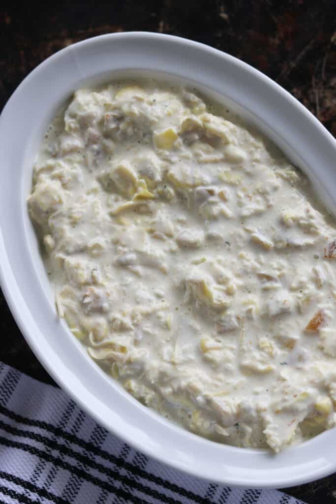 an artichoke dip with green chilies in a white dish about to go in the oven