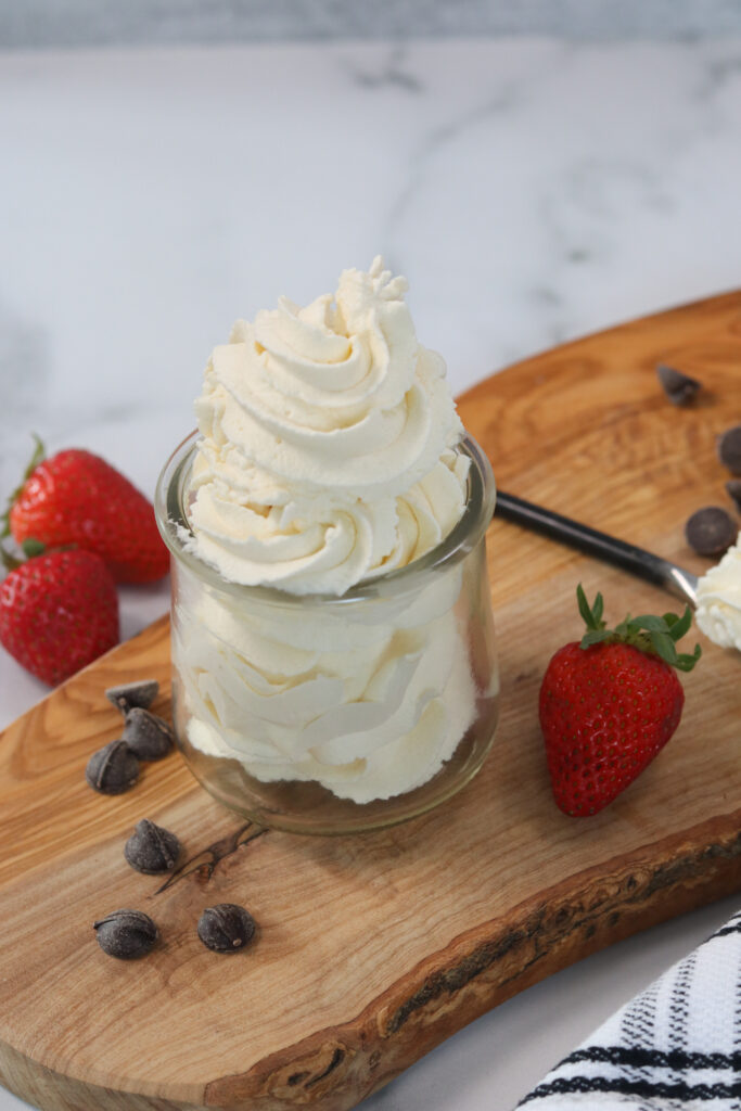 keto whipping cream in a clear jar on a cutting board next to strawberries and chocolate chips