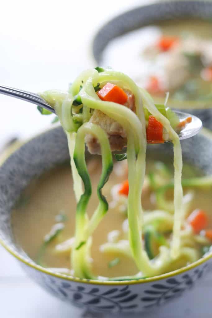 a bite of chicken zoodle soup on a spoon with zoodles hanging down