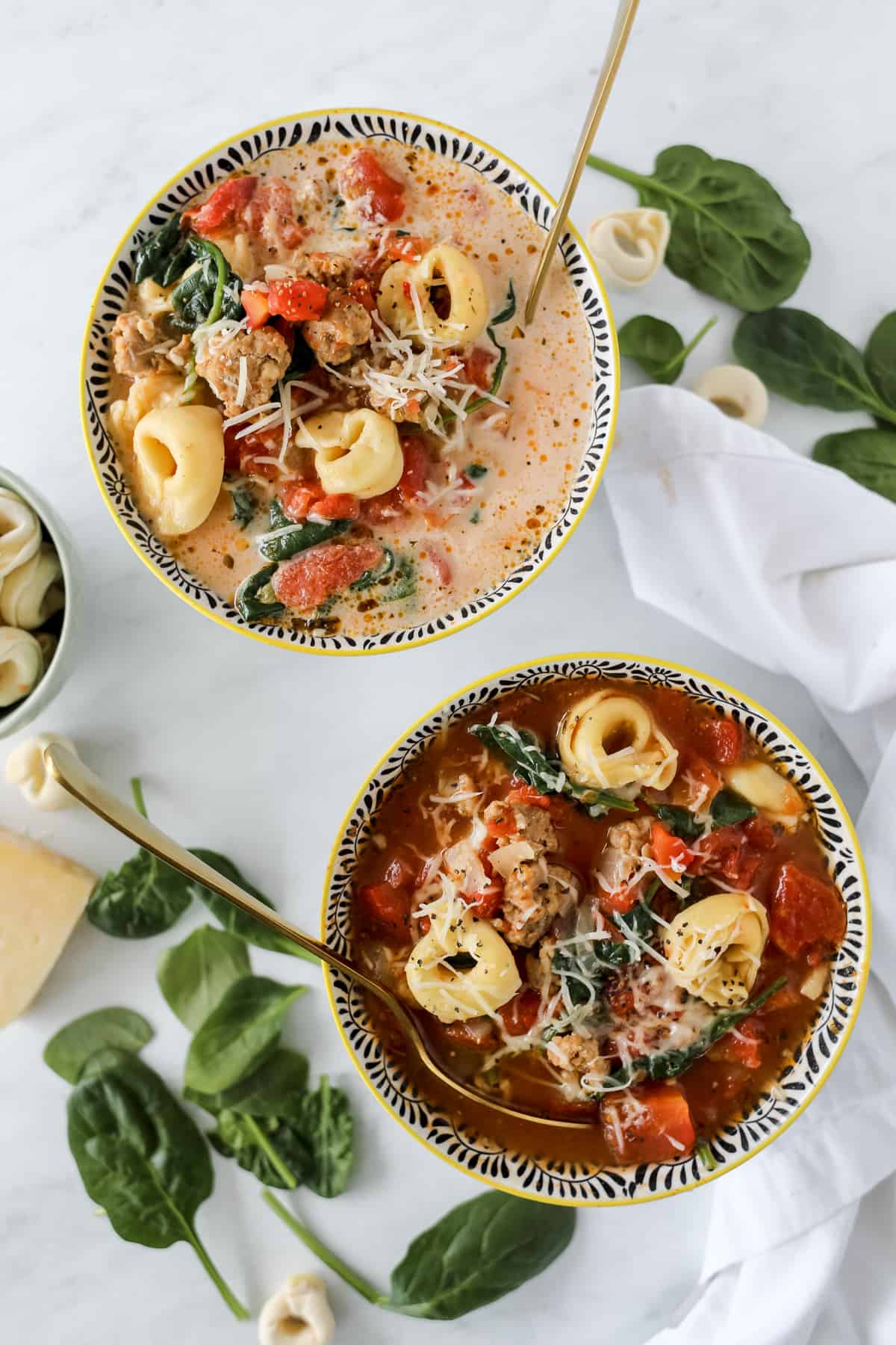 crock pot sausage tortellini soup with spinach in two bowls with parmesan garnish and spoons