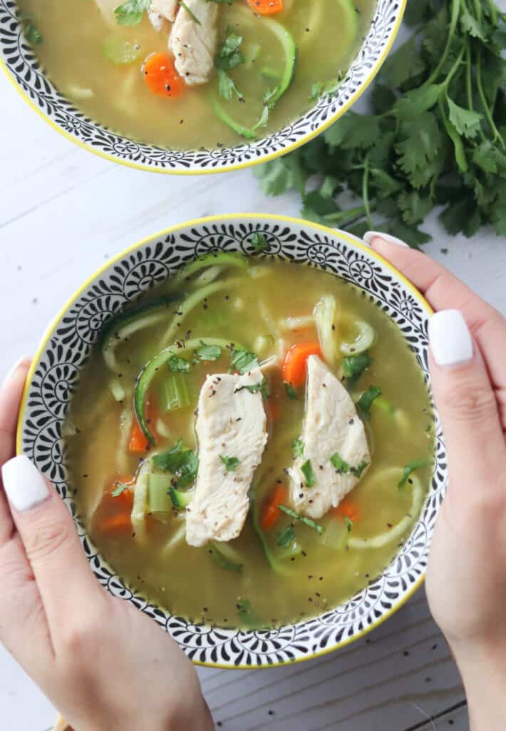 low carb chicken soup with hands on the side of the bowl on a white background