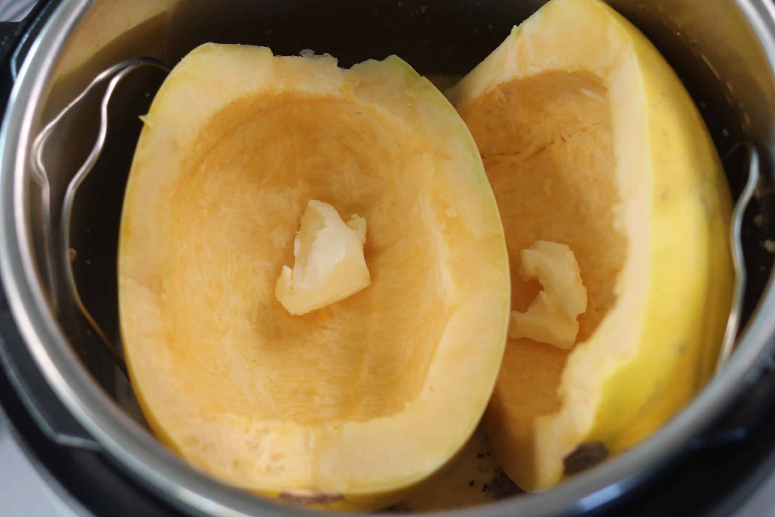 spaghetti squash halves in a pressure cooker with a pat of butter on top