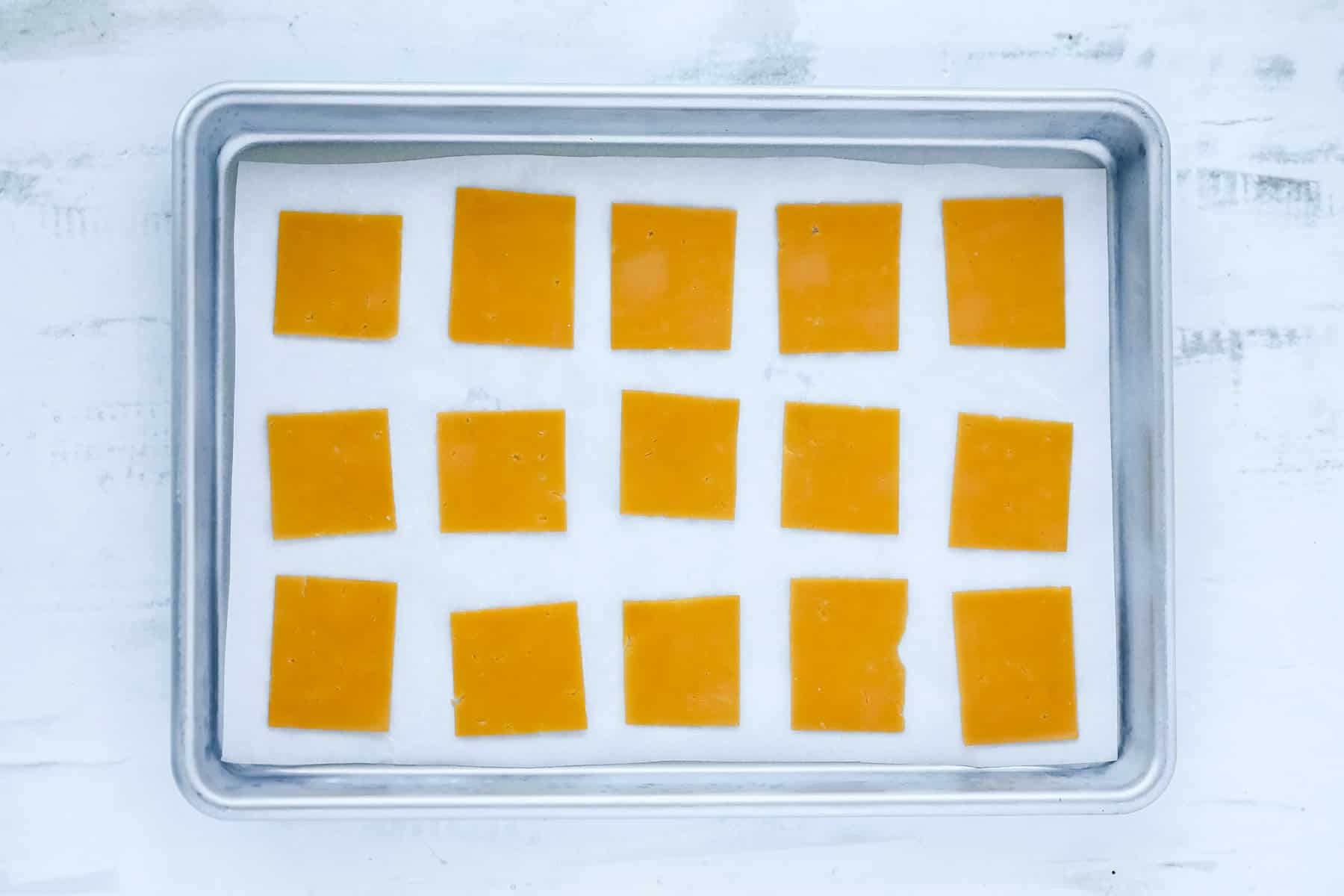 laying cheese slices on a baking sheet to bake in the oven