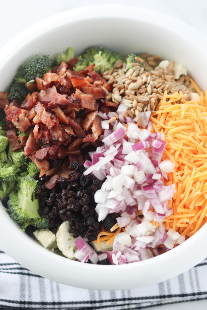 cauliflower broccoli salad ingredients in a white bowl before mixing or adding dressing