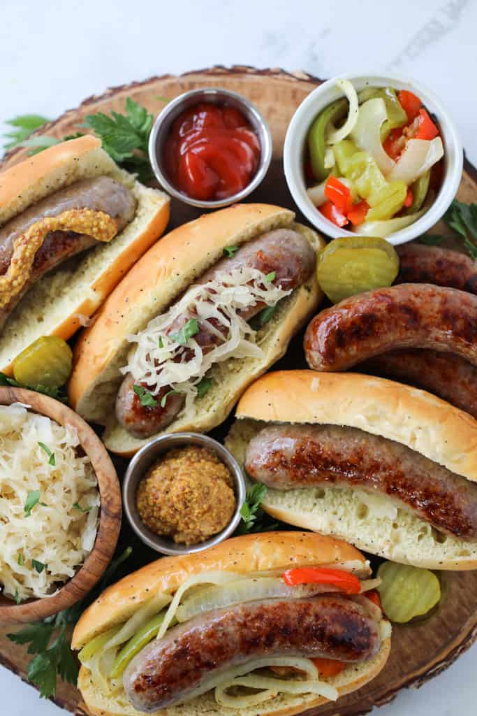 brats in oven on a wood tray with toppings
