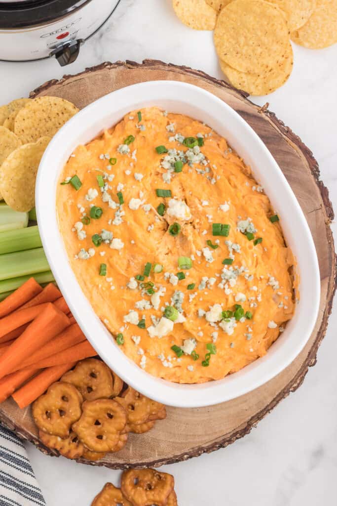 shredded buffalo chicken dip on a wood round with dippers such as carrots celery and pretzels and chips