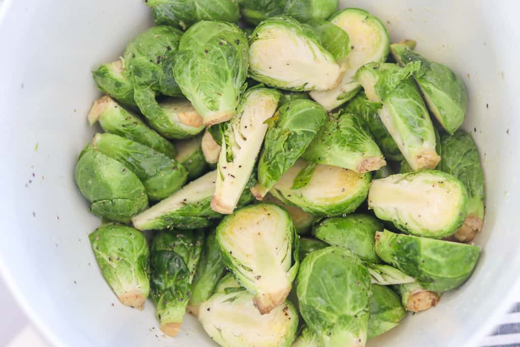 cut in half sprouts in a white bowl with seasoning