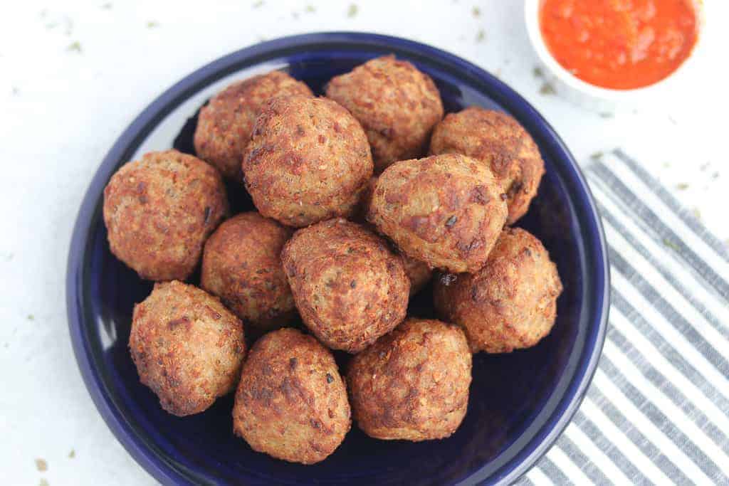 frozen meatballs in air fryer that are done cooking and on a blue plate next to marinara dipping sauce