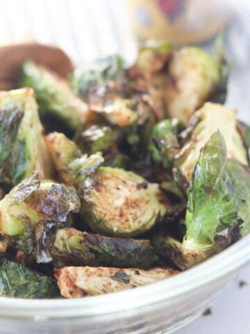 brussel sprouts in air fryer image after cooking in a clear glass bowl next to balsamic glaze