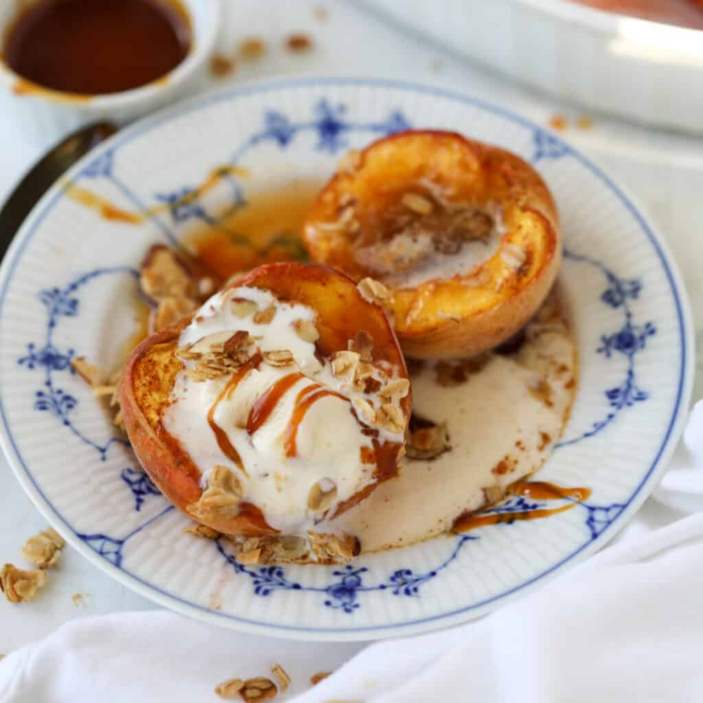 roast peaches on a white and blue plate with a scoop of vanilla ice cream