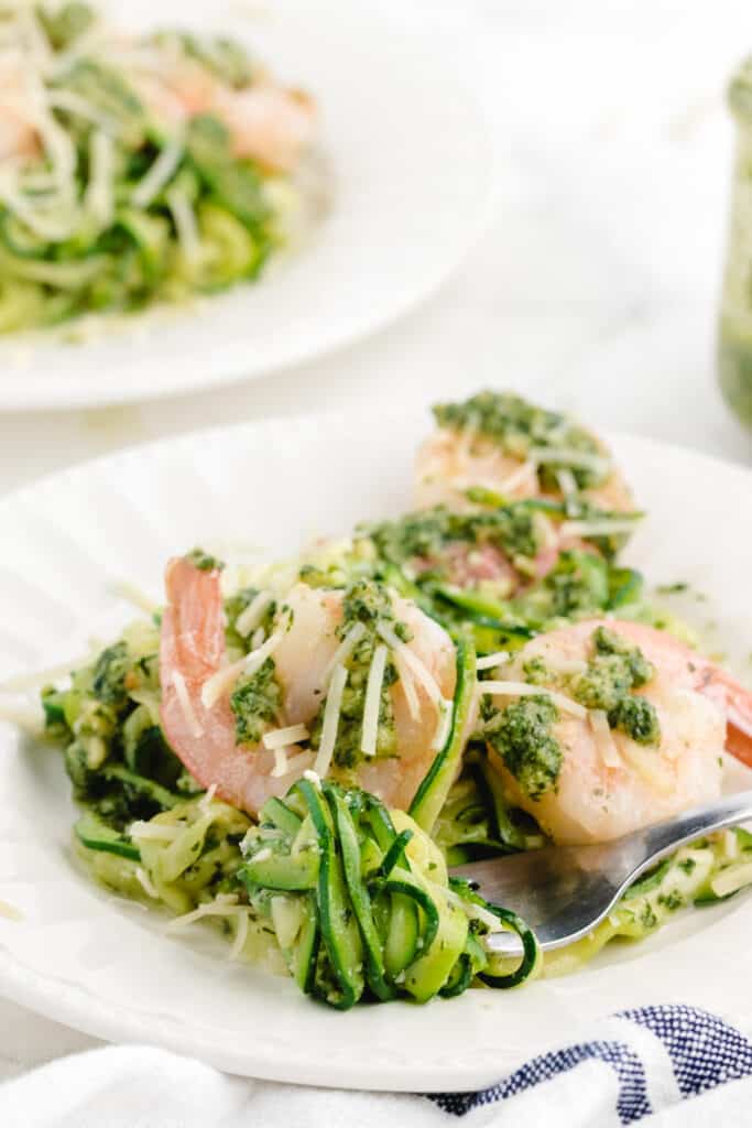 zucchini noodles with pesto shrimp and parmesan on a white plate