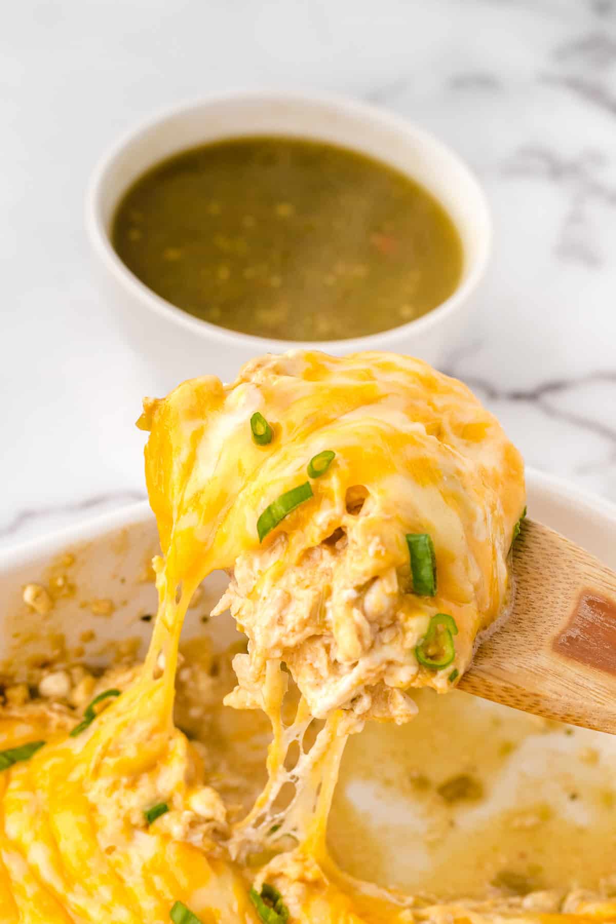 a wooden spoon of chicken casserole and a cheese pull 