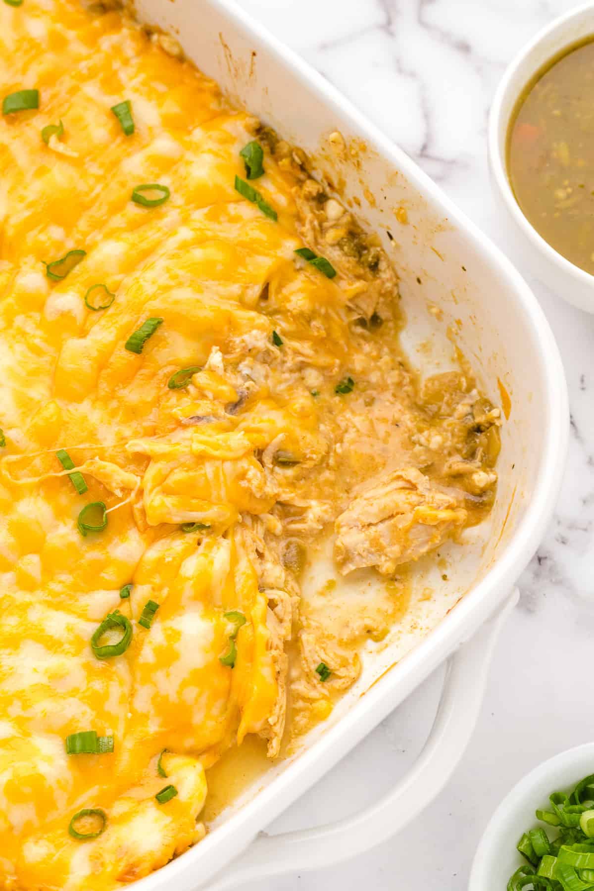 chicken chile casserole in a white baking dish with a spoon dished out of it