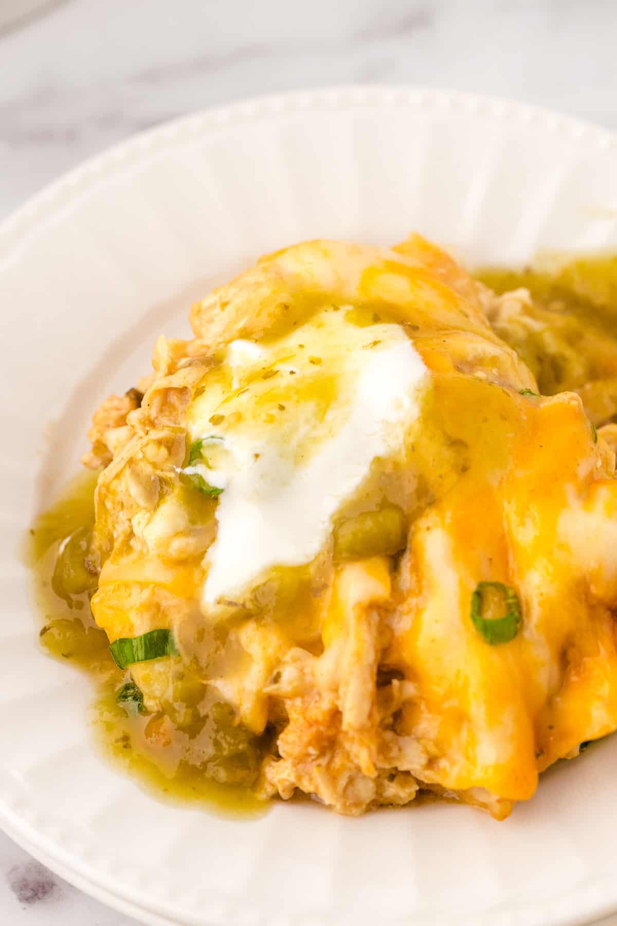 green chili casserole on a white plate topped with sour cream