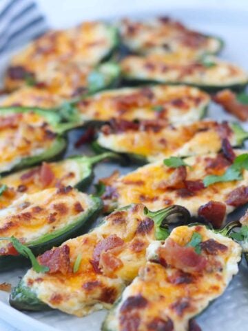 cooked jalapeno poppers on a white plate with bacon crumbled on top