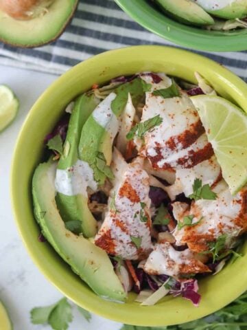 fish taco bowl with avocado and limes in a green bowl