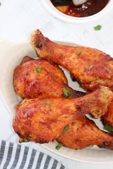 air fryer drumsticks with BBQ sauce on a plate next to sauce