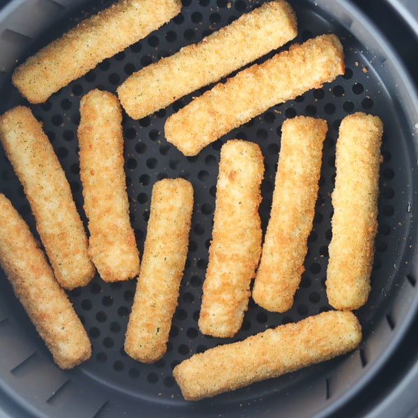 frozen mozzarella sticks in an air fryer basket ready to cook