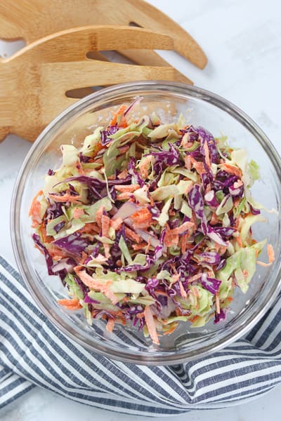 a healthy slaw recipe mixed in a bowl with serving tongs