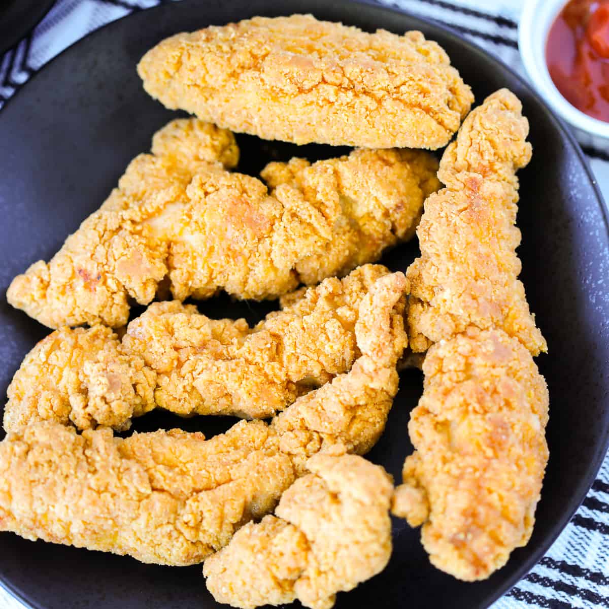 frozen chicken tenders in air fryer on a plate next to ketchup