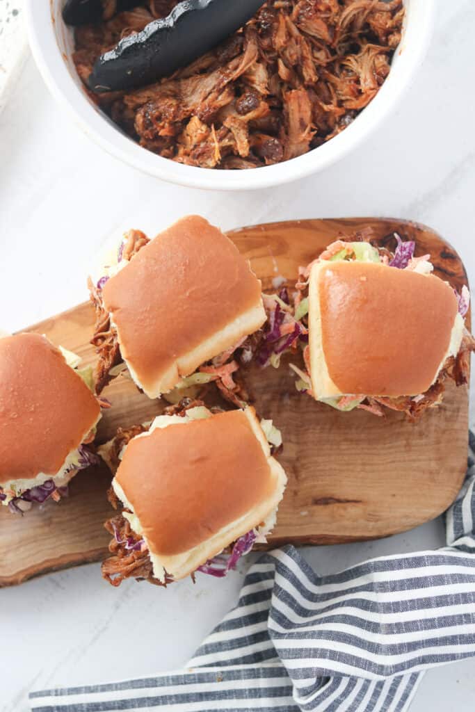 hawaiian pulled pork sliders top down view with the sliders on a cutting board next to a bowl of pulled pork