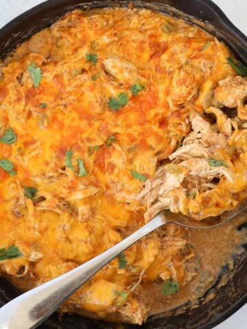 sour cream enchilada casserole in a skillet with a spoon of cheesy chicken