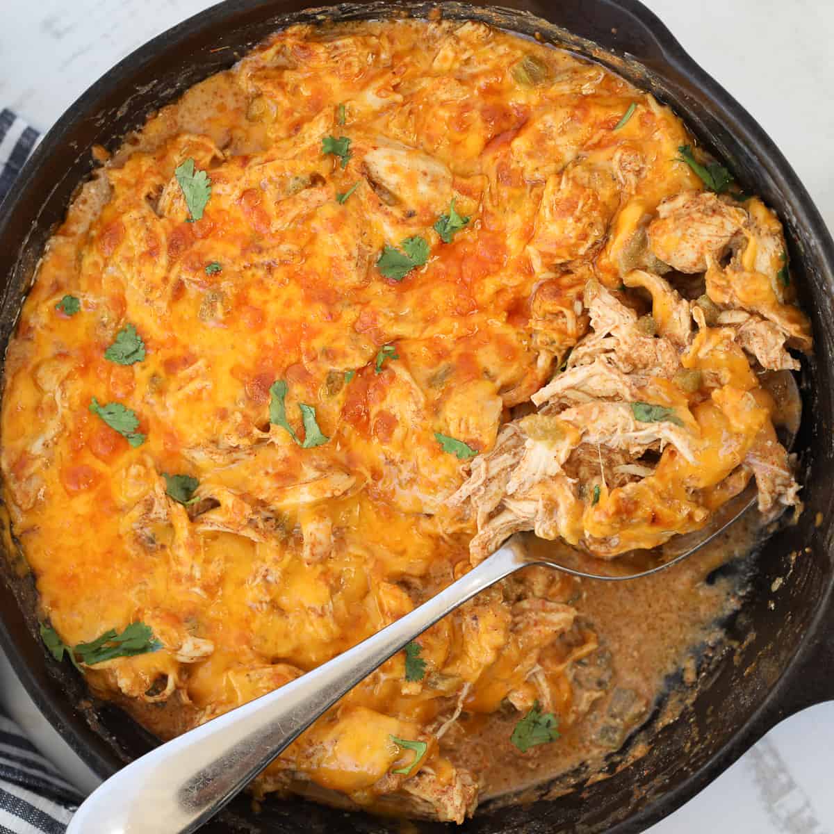 sour cream enchilada casserole in a skillet with a spoon of cheesy chicken