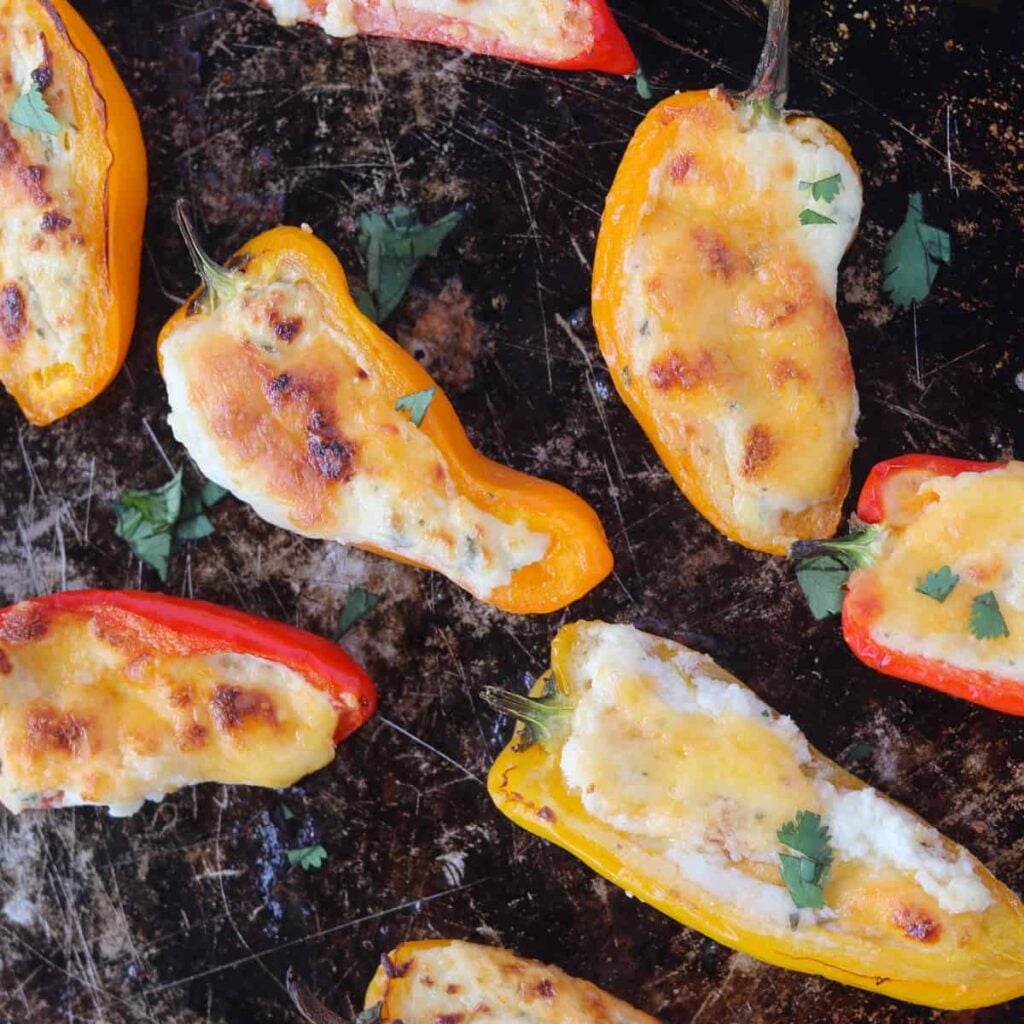 stuffed mini sweet peppers on a baking sheet after cooking with melted cheese