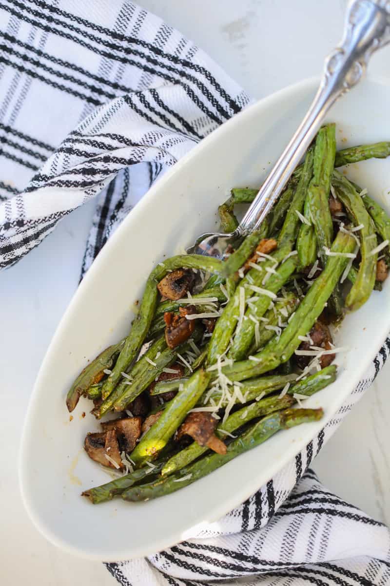 air fryer green beans top down view after cooking in a white bowl with a spoon on a white background