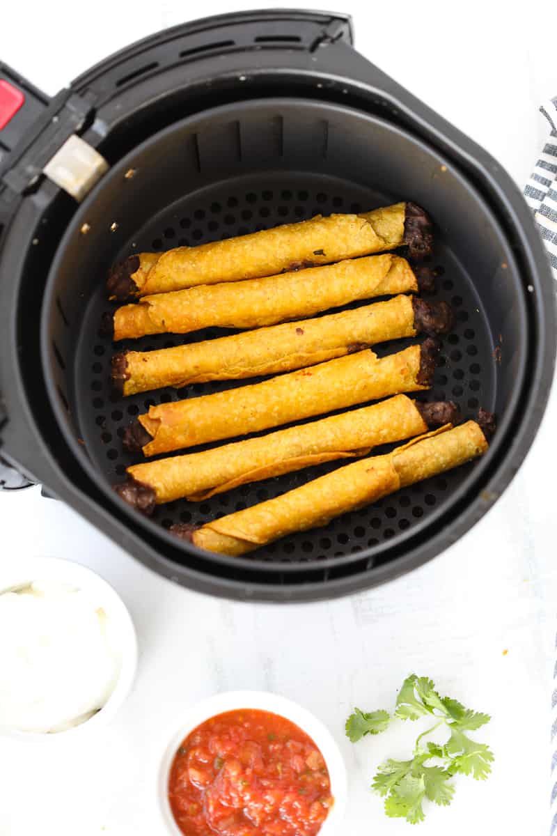air fryer taquitos in a farberware basket style air fryer after cooking with salsa and sour cream in dishes on the side