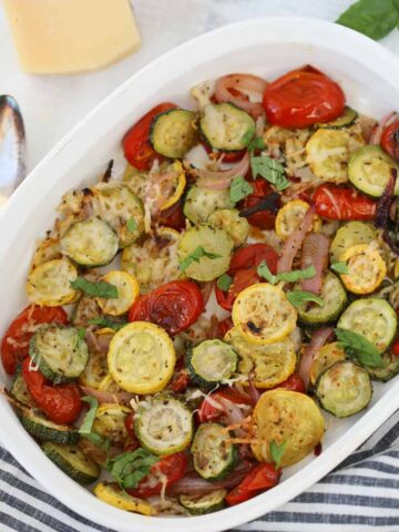 baked zucchini and squash with cheese in a white pan on a striped cloth background