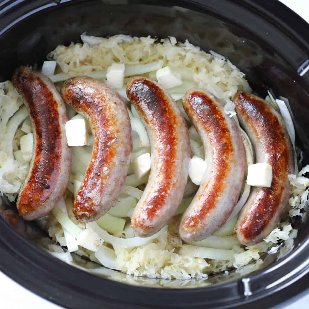 laying the crockpot brats on top of the sauerkraut and dotting with butter