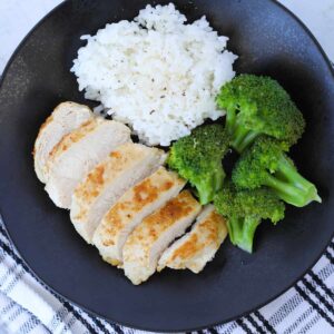 frozen chicken breast air fryer recipe after cooking served sliced on a plate with broccoli and rice