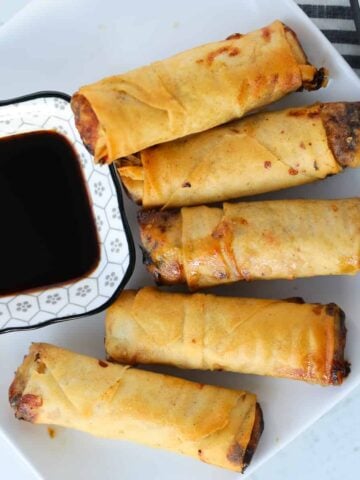 frozen egg rolls in air fryer on a white plate with soy sauce