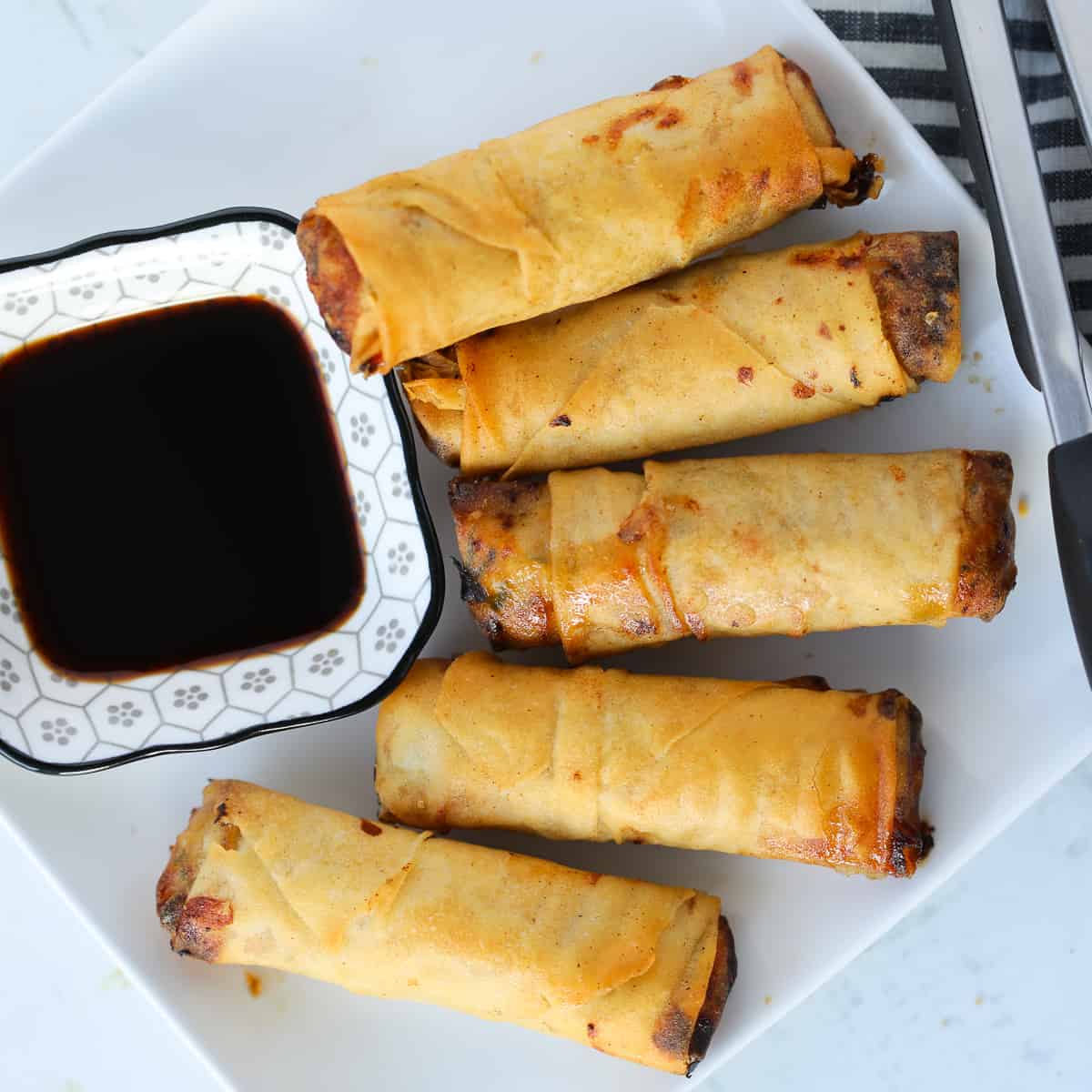 frozen egg rolls in air fryer on a white plate with soy sauce