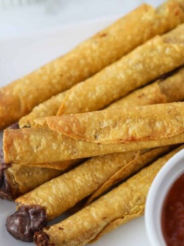 frozen taquitos in air fryer after cooking with dipping sauce on a white plate