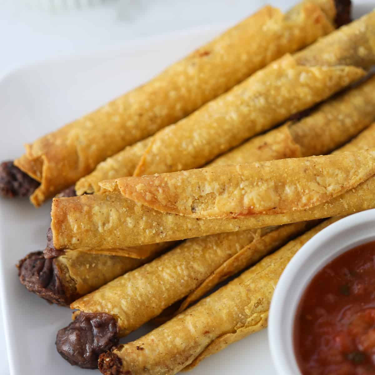 frozen taquitos in air fryer after cooking with dipping sauce on a white plate