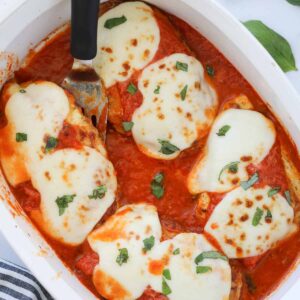 keto chicken parmesan in a baking dish with a spatula under one piece of chicken