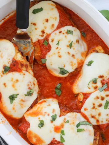 keto chicken parmesan in a baking dish with a spatula under one piece of chicken