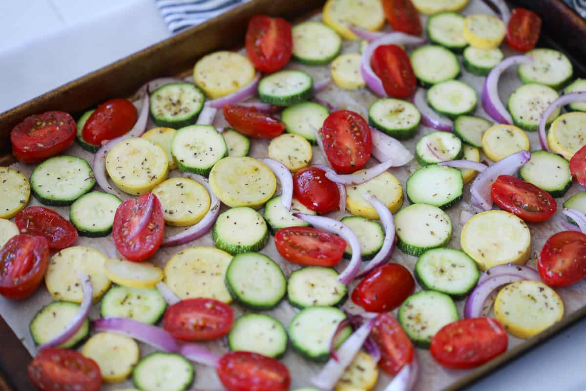 roasted zucchini and squash and onions spread on a pan before getting baked in the oven